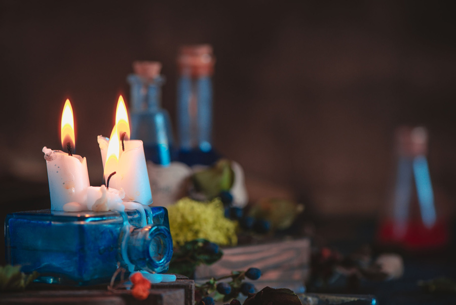 Candles burn low and bottles of potions in the background.